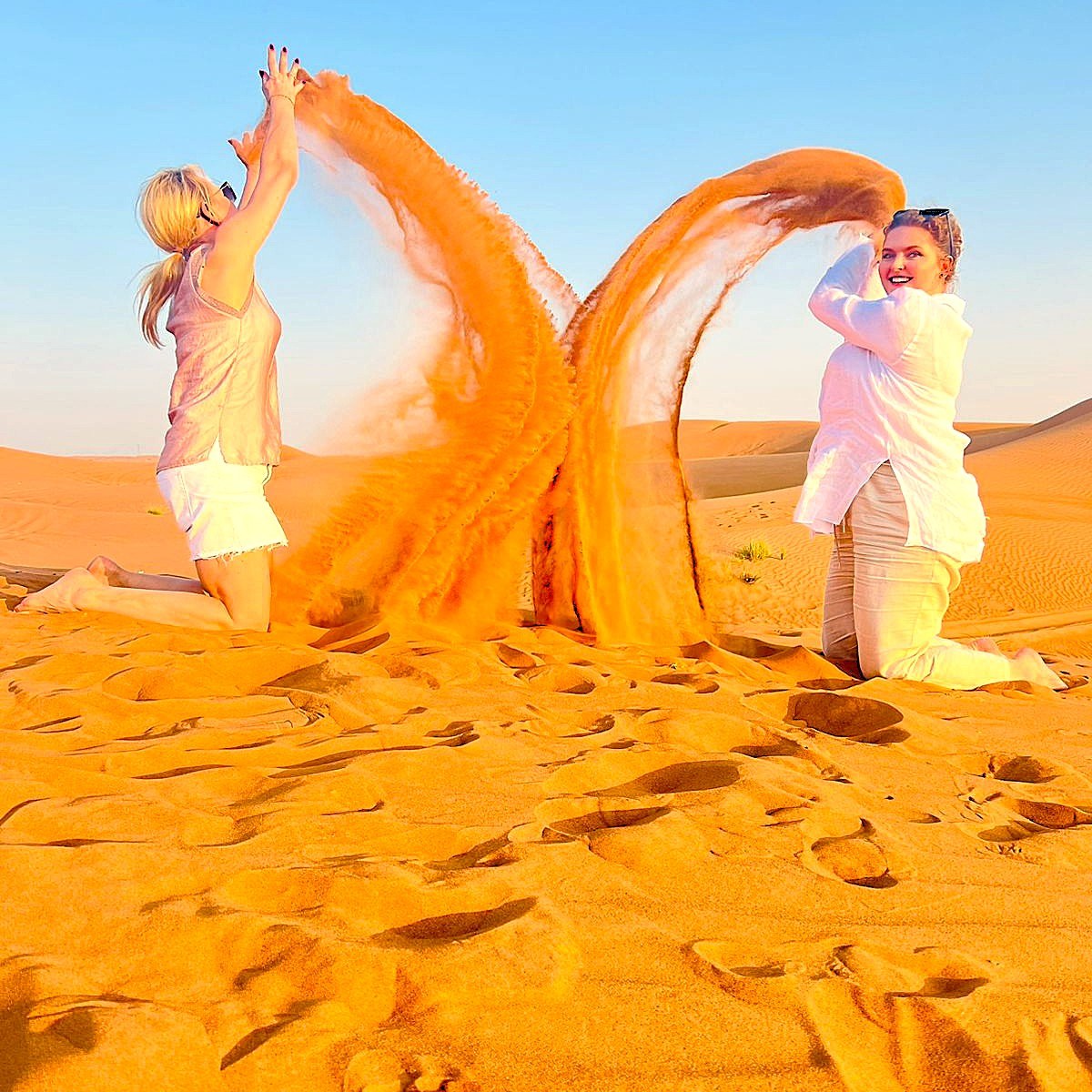 Two guests creating a heart shape by throwing sand at sunset in the Dubai desert