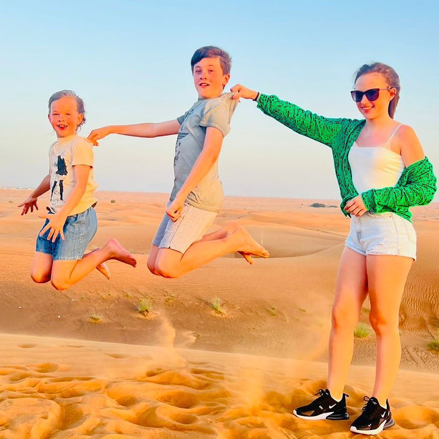 Three siblings jumping together on a dune at sunset