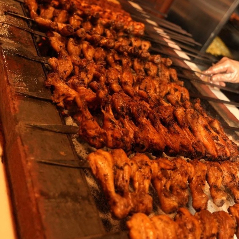 Chicken skewers grilling over charcoal at a Dubai desert safari camp
